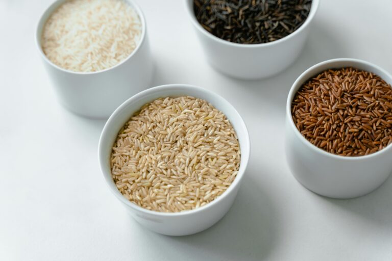 Four types of rice grains displayed in white ceramic bowls on a white background.